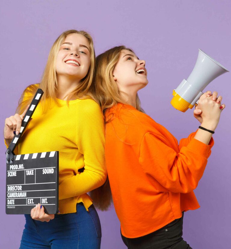 Two teenage girl acting students one holding a clapper board and the other holding a mega phone